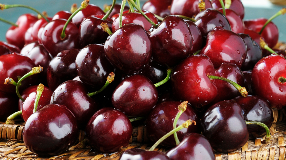 Mucchio di ciliegie di Vignola IGP scure e lucide in un cesto di vimini.
