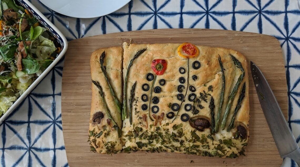 focaccia decorata con ortaggi su tagliere di legno e sfondo piastrellato