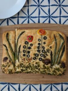 focaccia decorata con ortaggi su tagliere di legno e sfondo piastrellato