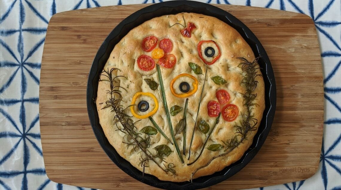 focaccia fiorita in una teglia tonda su tagliere di legno