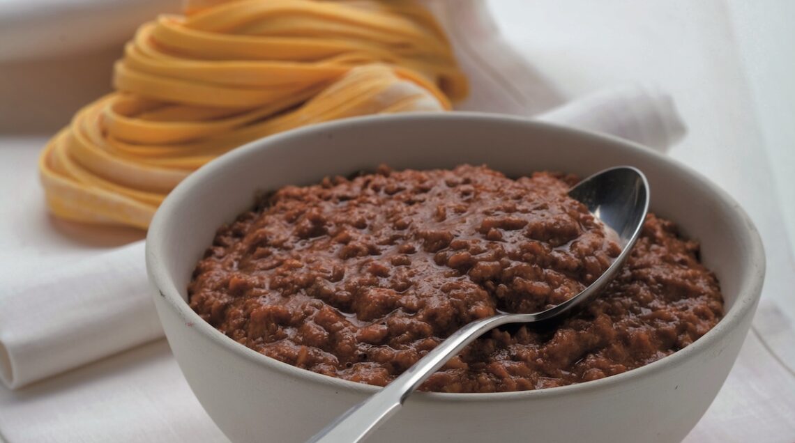 Una ciotola di ragù accanto a matassine di tagliatelle