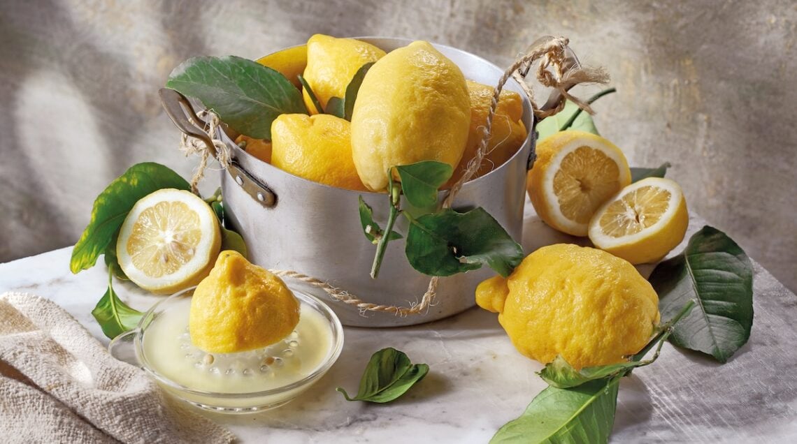limoni interi, tagliati e spremuti su un tavolo e in una pentola