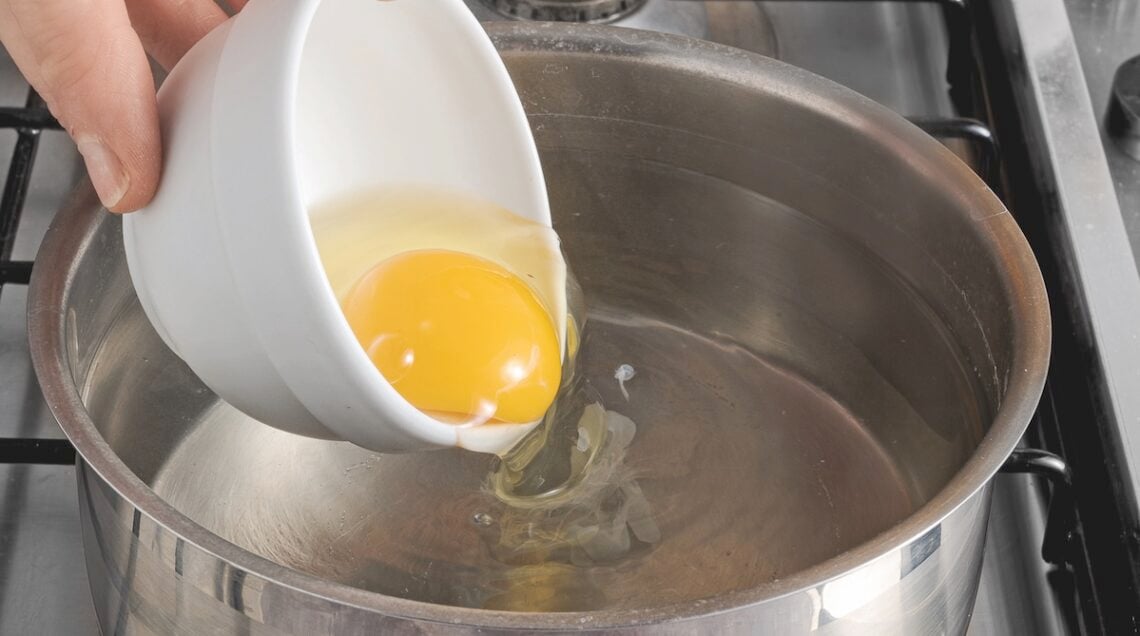 uovo che scivola da una ciotolina all'acqua bollente per la cottura in camicia