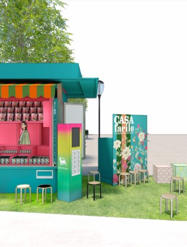 Rendering architettonico di un'edicola pop-up color verde ottanio con scaffali rosa e area relax esterna su prato sintetico.