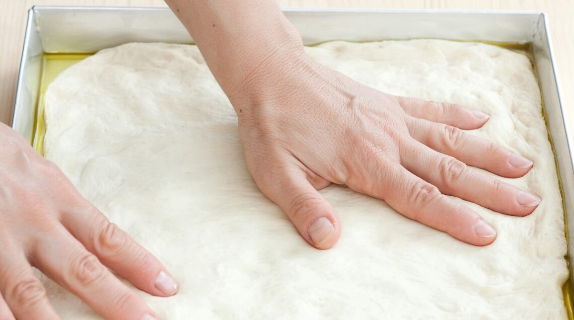 mani che stendono l'impasto in una teglia