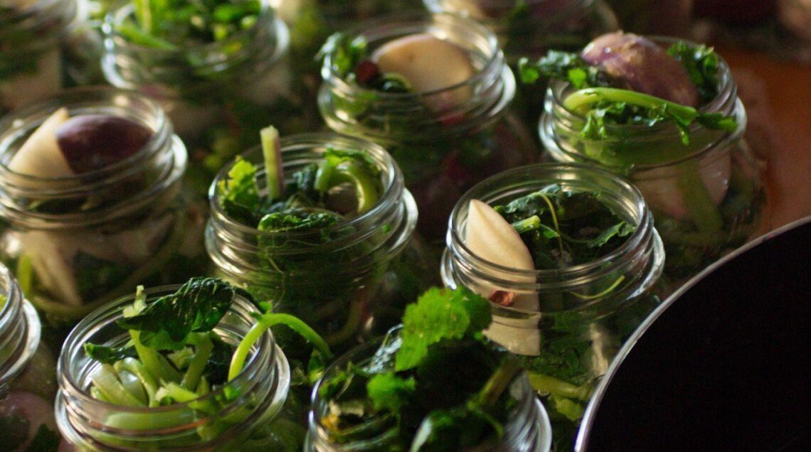 Serie di vasetti di vetro in fase di riempimento con rape e aromi per la produzione di Pestith artigianale