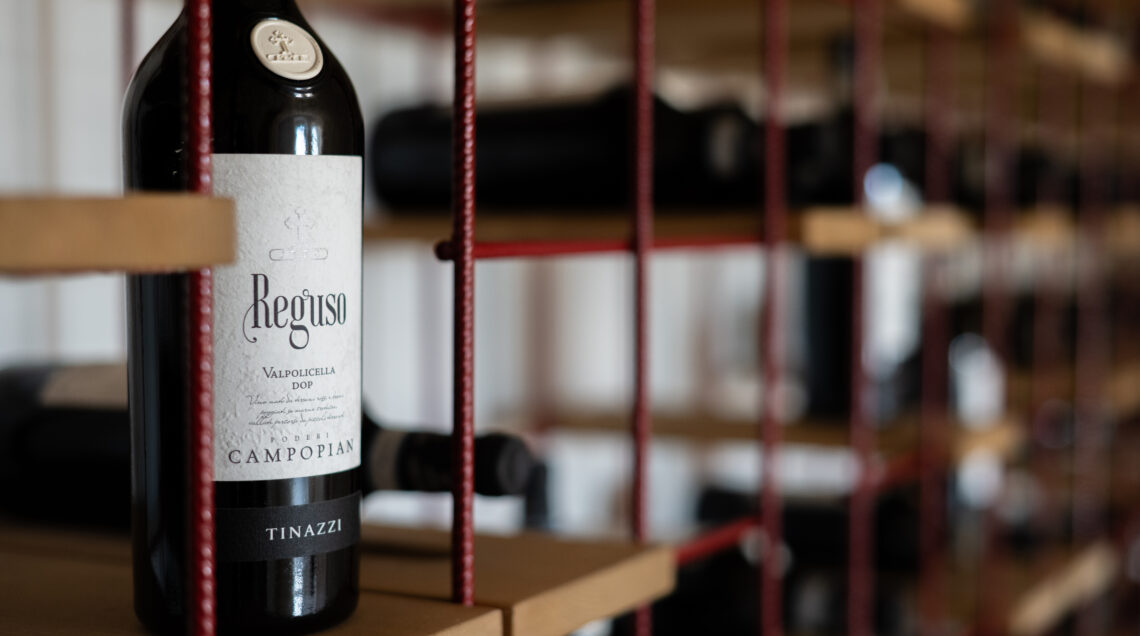 Primo piano di una bottiglia di vino Reguso Valpolicella DOP di Poderi Campopian Tinazzi su uno scaffale di design. 