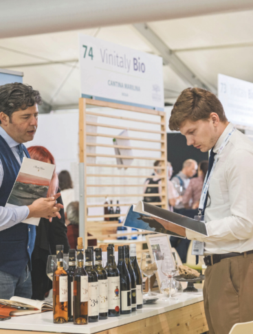 Visitatori e produttori presso lo stand Vinitaly Bio a Veronafiere durante l'edizione 2026, con esposizione di bottiglie di vino biologico toscano e brochure informative