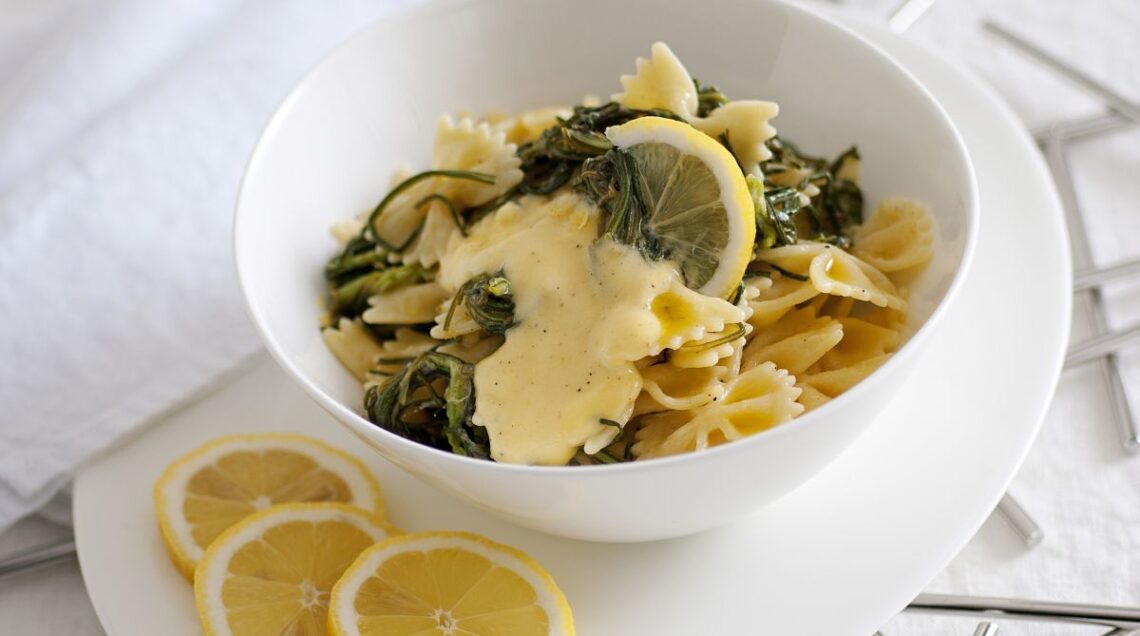 piatto di farfalle agli agretti con crema di uova e limone, in una ciotola di ceramica con adagiate vicino tre fettine di limone