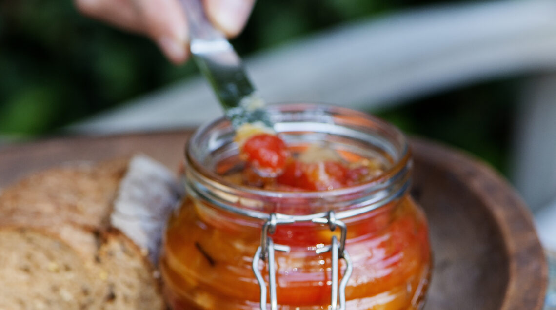 vasetto di vetro che contiene chutney di anguria, con persona che lo spalma con un coltello su una fetta di pane