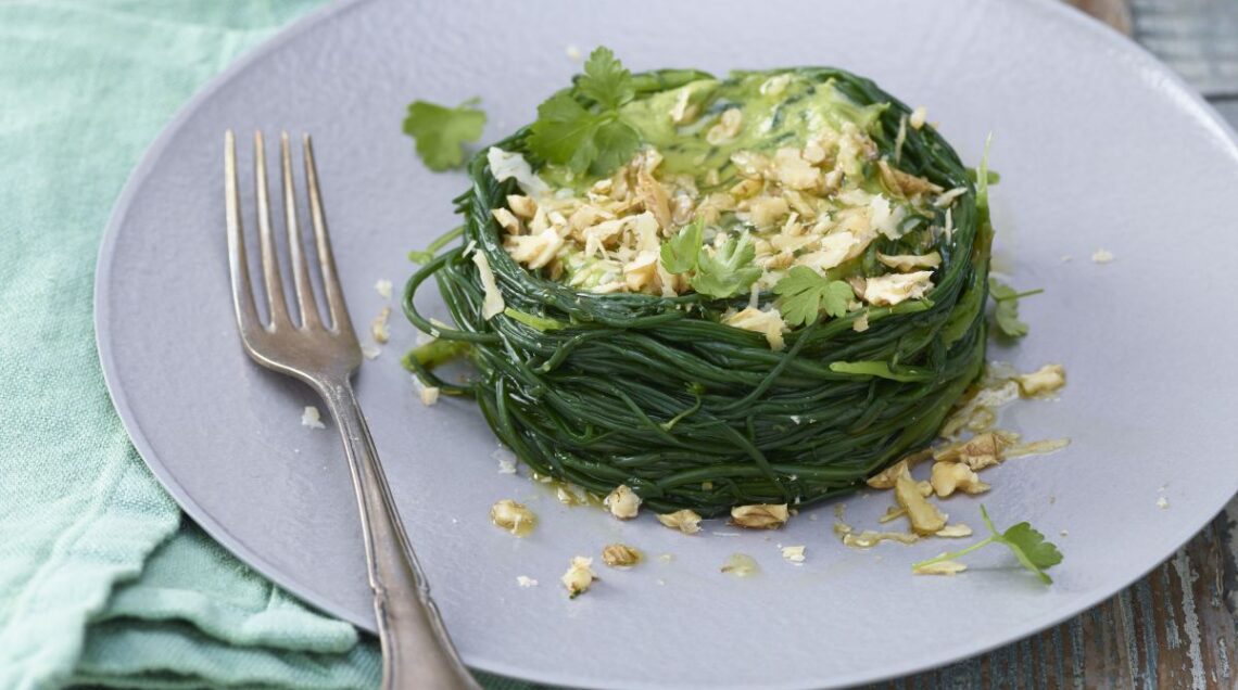 tortino di agretti con in cima guacamole e noci con una forchetta a lato, disposto su un piatto su un tavolo