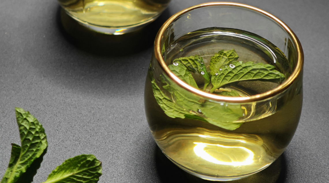 Due bicchieri di vetro con bordo dorato contenenti un infuso freddo dorato e foglie di menta fresca.