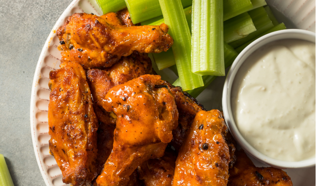Buffalo Wings pronte da gustare, ricoperte di salsa piccante e servite con dip al formaggio in una ciotola e bastoncini di sedano