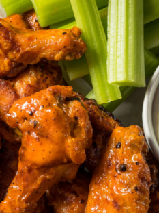 Buffalo Wings pronte da gustare, ricoperte di salsa piccante e servite con dip al formaggio in una ciotola e bastoncini di sedano