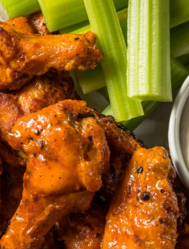 Buffalo Wings pronte da gustare, ricoperte di salsa piccante e servite con dip al formaggio in una ciotola e bastoncini di sedano