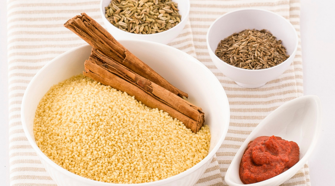 Una ciotola di cous cous con cannella. a fianco ciotoline di harissa, semi di carvi e cumino