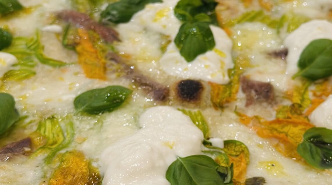 pizza con fiori di zucca, acciughe e mozzarella, dal bordo basso e bruciacchiato