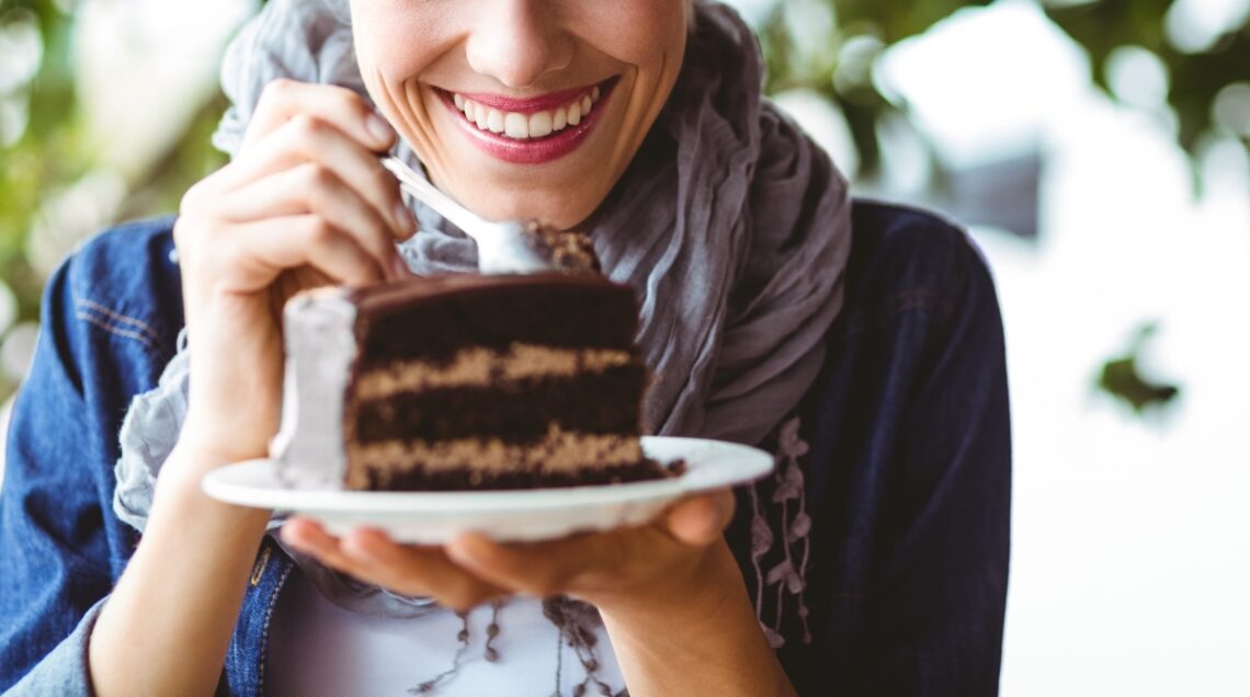 Donna sorridente che tiene in mano una grande fetta di torta al cioccolato su un piatto, pronta a tuffarvi il cucchiaio