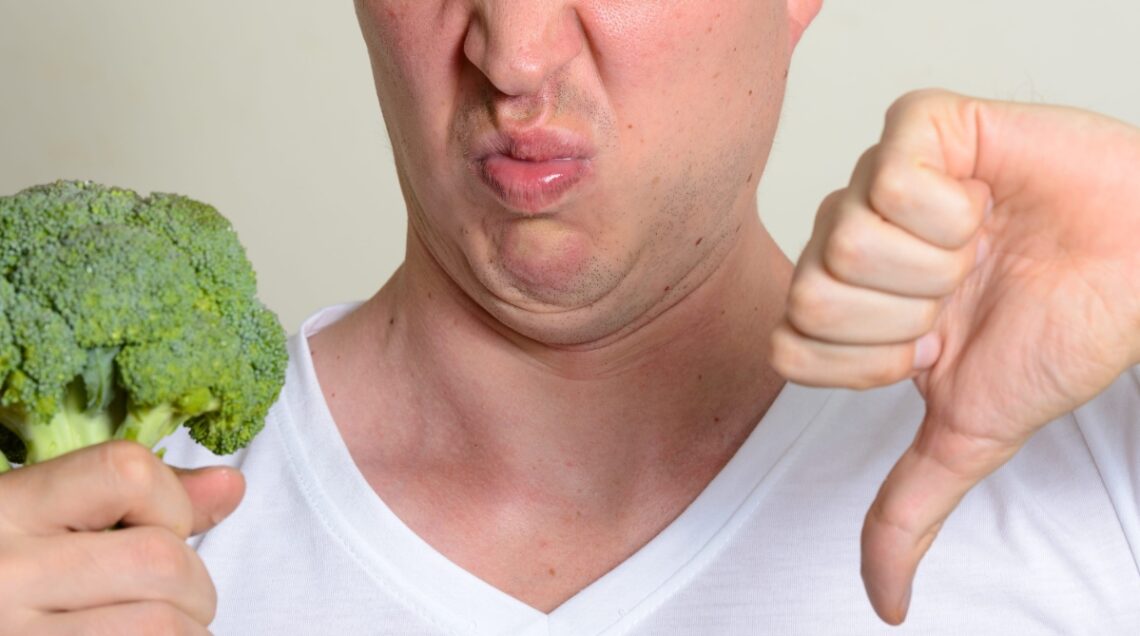 Uomo che storce la bocca davanti a dei broccoli freschi e fa il pollice verso