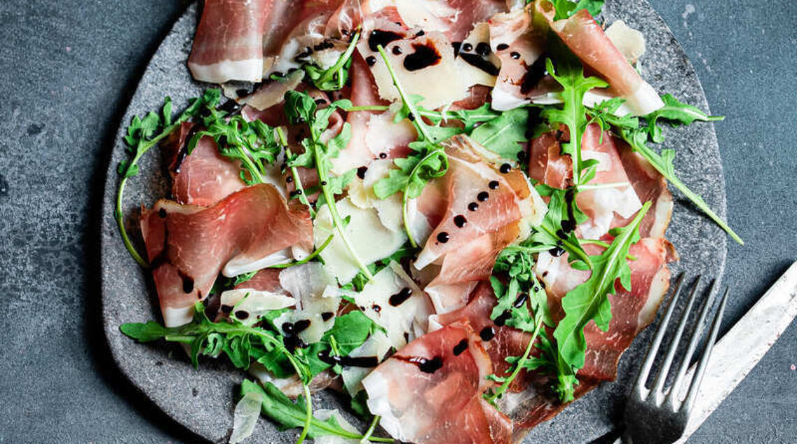 piatto di fette di speck, scaglie di grana, foglie di rucola e cialde di segale