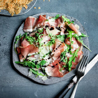 piatto di fette di speck, scaglie di grana, foglie di rucola e cialde di segale
