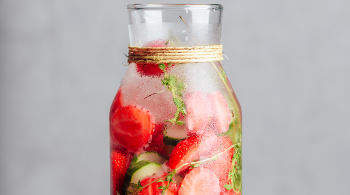 Bottiglia in vetro con acqua aromatizzata fredda, fragole a fette, cetrioli e rametti di timo.