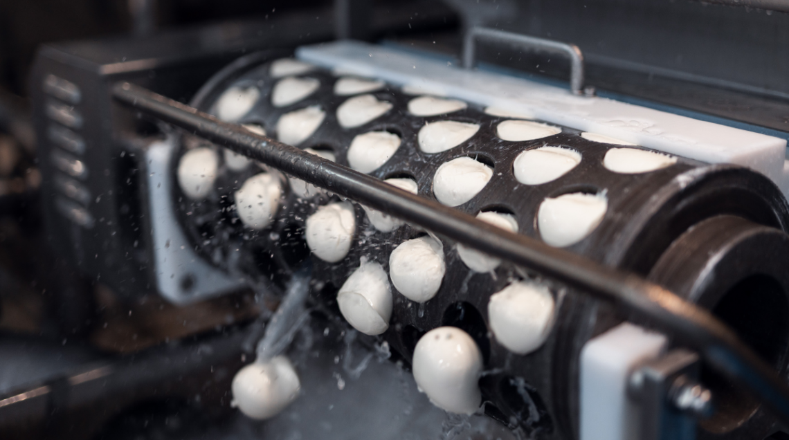 Macchinario industriale che modella mozzarelle sferiche durante il processo di produzione.