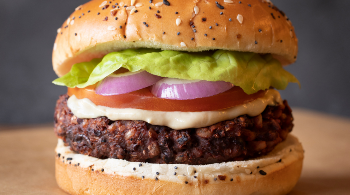 Un hamburger gourmet con maionese, fetta di pomodoro, anelli di cipolla rossa e lattuga in un panino con semi di sesamo e papavero.