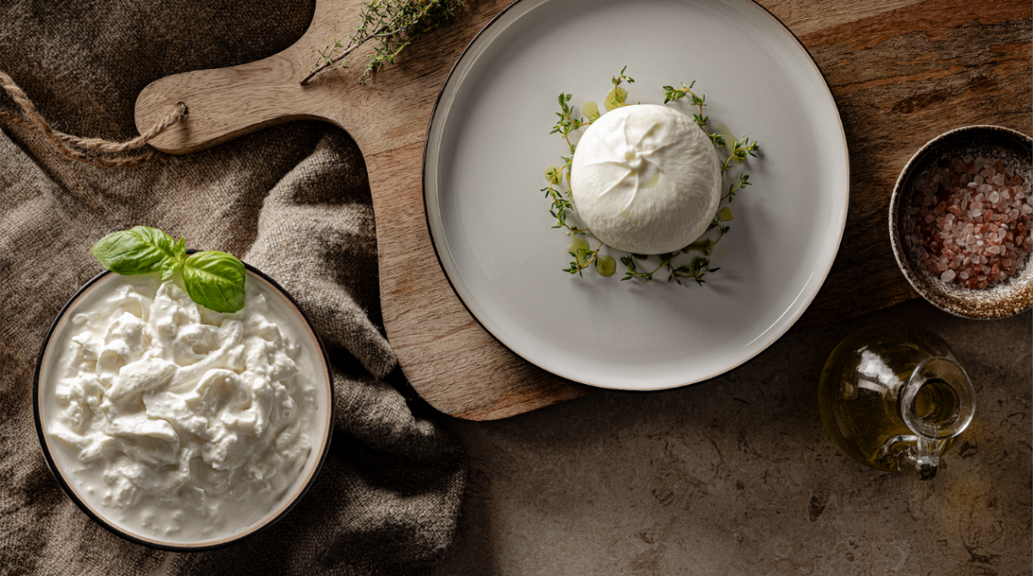 Vista dall'alto di una burrata su un piatto bianco e una ciotola di stracciatella fresca con basilico.