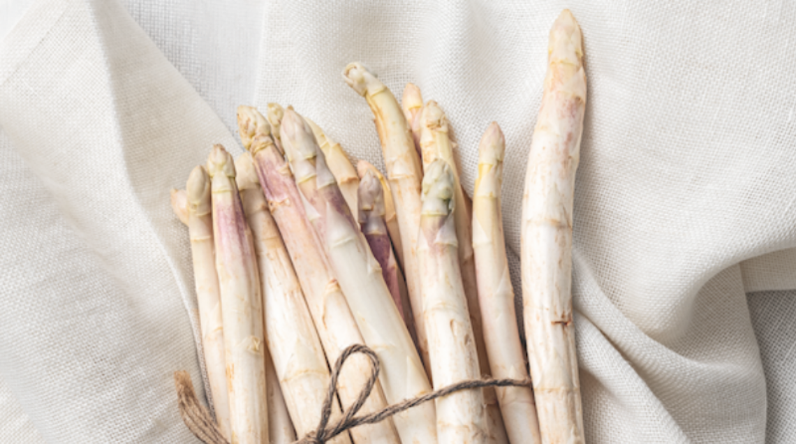 Mazzo di asparagi bianchi freschi legati con uno spago rustico, adagiati su un tovagliolo di lino bianco stropicciato.