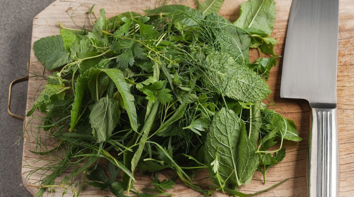 erbe aromatiche miste su un tagliere di legno con coltello accanto