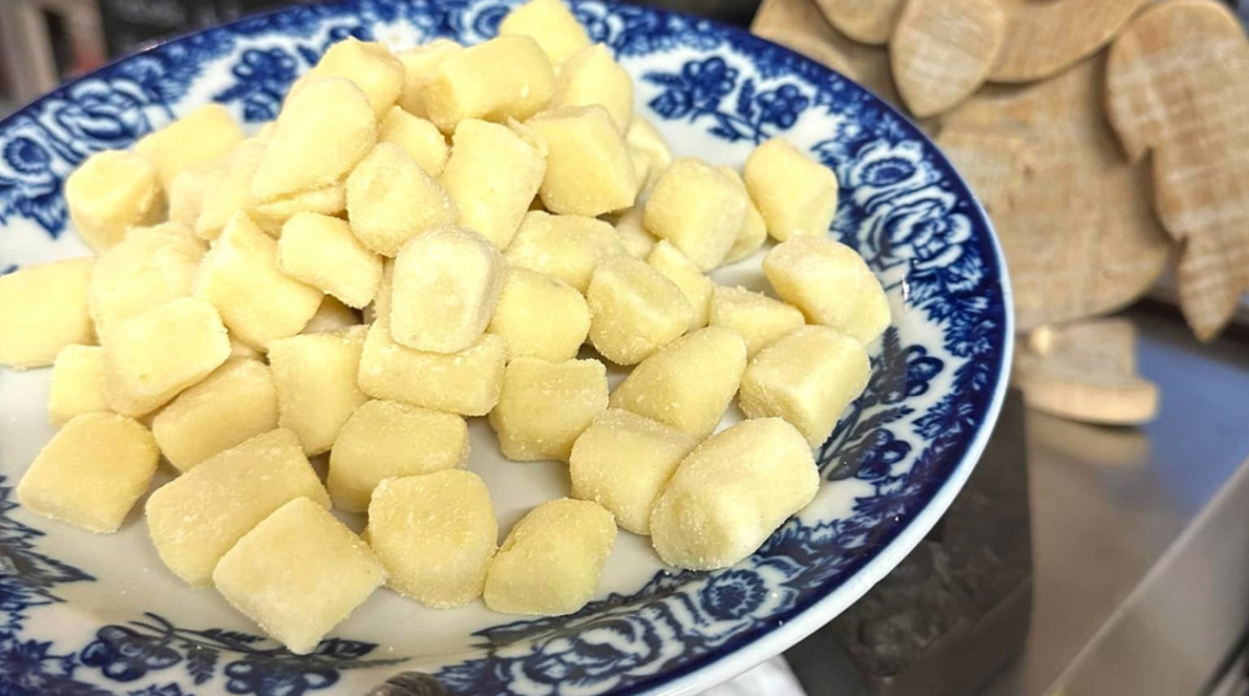 Un piatto di gnocchi di patate conditi con crema di Castelmagno accanto a una civetta in legno. 