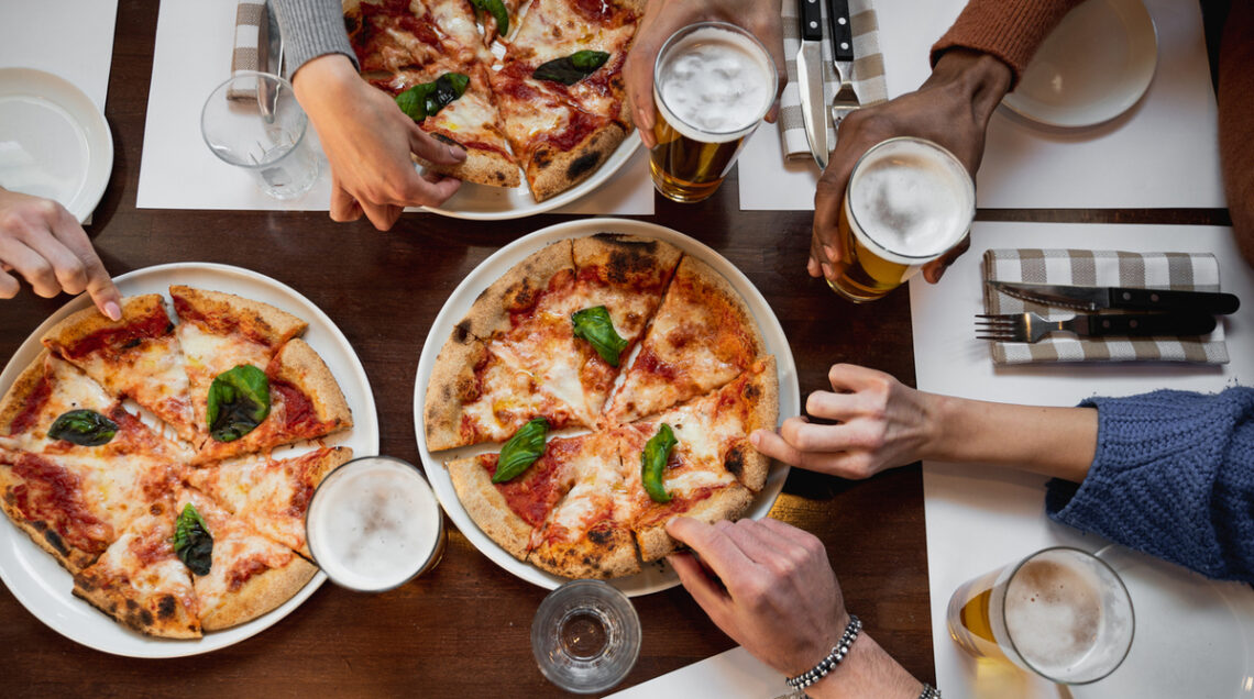 vista dall'alto di una tavola apparecchiata con piatti di pizza tagliata a fette e mani di persone