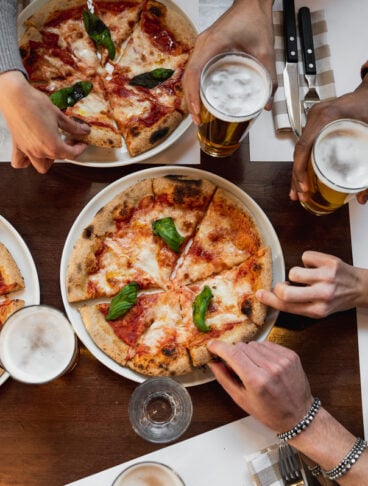 vista dall'alto di una tavola apparecchiata con piatti di pizza tagliata a fette e mani di persone