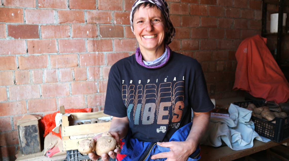 Una donna sorridente tiene in mano alcune patate di montagna in un magazzino agricolo.
