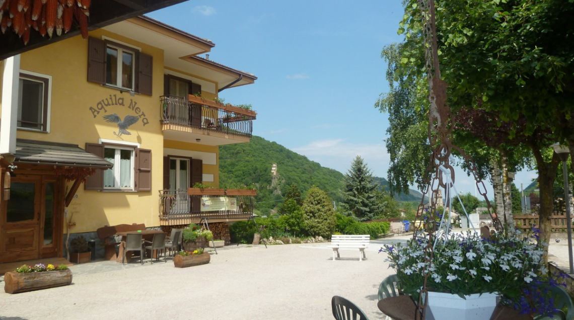 Facciata gialla dell'Osteria Aquila Nera a Monterosso Grana con tavoli all'aperto. 