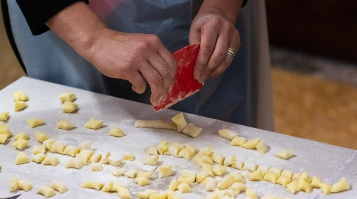 Mani che lavorano l'impasto per preparare gli gnocchi di patate su una superficie infarinata.
