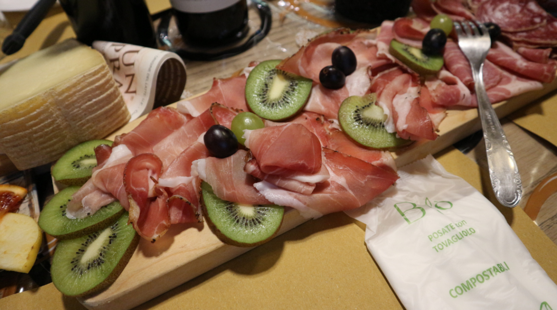 Tagliere in legno con salumi locali, fette di kiwi, uva e formaggi della Valle Grana. 