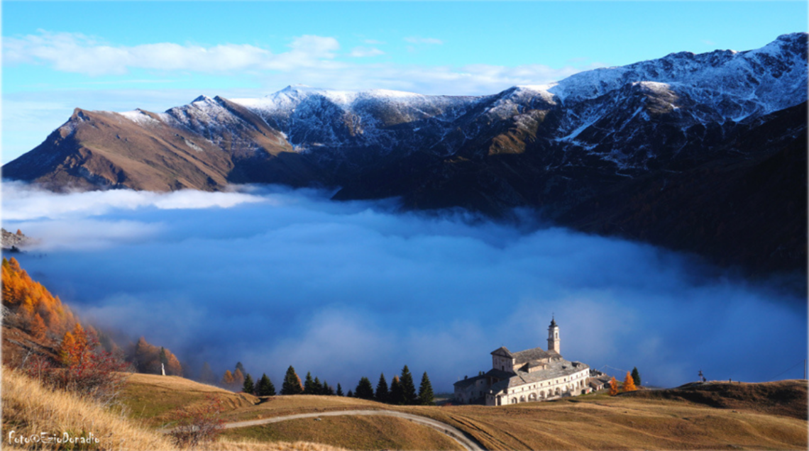 Il Santuario di San Magno che emerge dalle nuvole in un paesaggio alpino d'alta quota. 