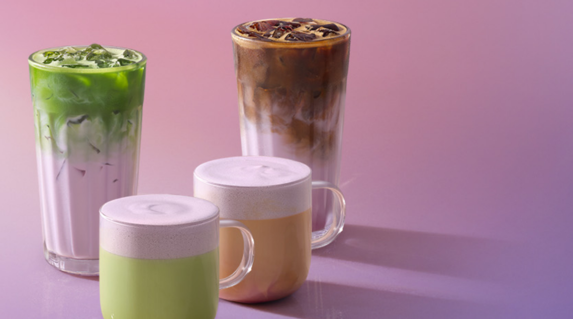 Selezione di bevande calde e fredde color lilla a base di ube e matcha, servite in bicchieri di vetro e tazze in ceramica