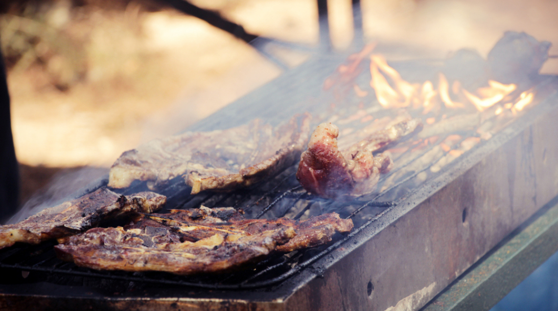 Grosse bistecche e grandi pezzi di carne vengono cotti su un grande grill in stile americano, su fiamma e carboni ardenti