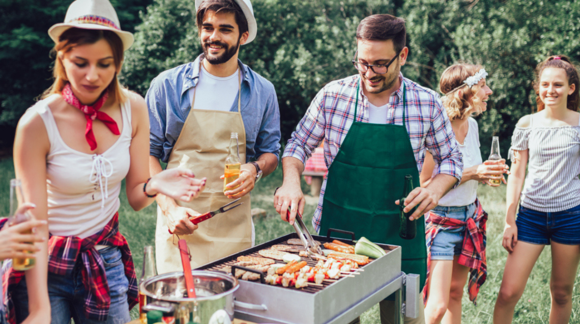 Un gruppo di amici fanno il barbecue all'aperto, due amici curano il grill e gli altri scherzano