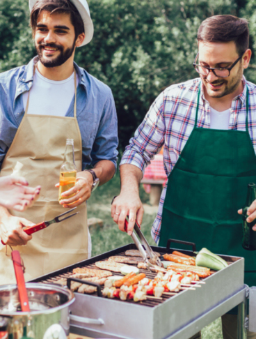 Un gruppo di amici fanno il barbecue all'aperto, due amici curano il grill e gli altri scherzano