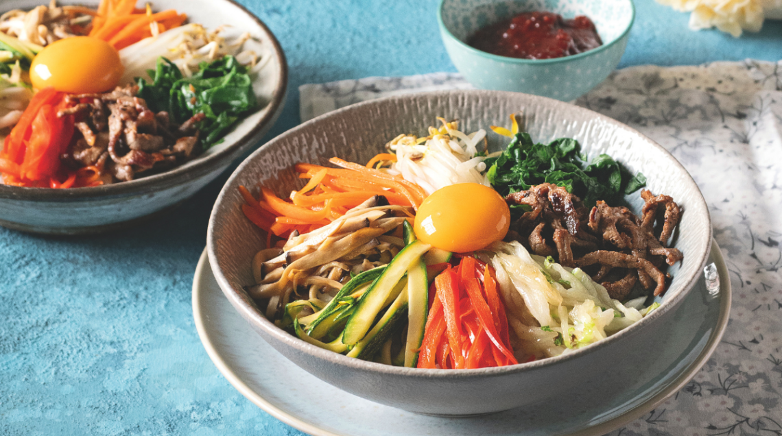 due ciotole di bibimbap e una piccola ciotola di salsa gochujang su una superficie piana turchese