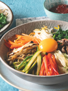 due ciotole di bibimbap e una piccola ciotola di salsa gochujang su una superficie piana turchese