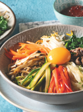 due ciotole di bibimbap e una piccola ciotola di salsa gochujang su una superficie piana turchese