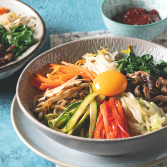 due ciotole di bibimbap e una piccola ciotola di salsa gochujang su una superficie piana turchese