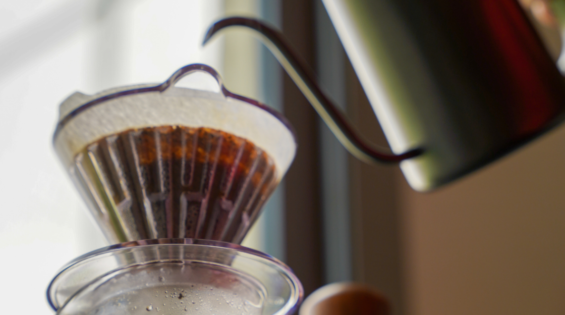 Dettaglio ravvicinato dell'acqua calda versata sul caffè macinato all'interno di un filtro conico di carta.