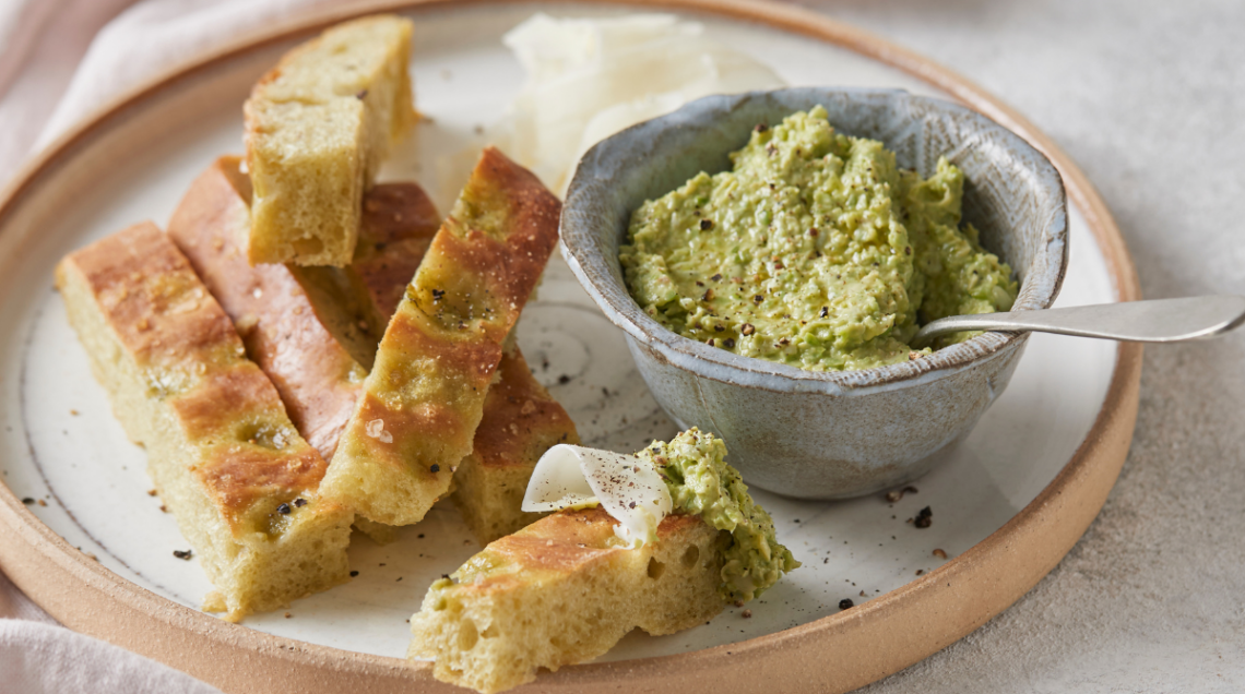 Strisce di focaccia dorata guarnite con sale grosso e una ciotolina con una crema di fave e un cucchiaio