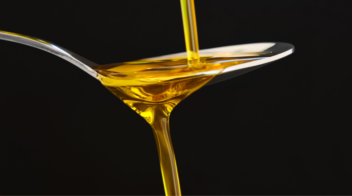 Olio extravergine di oliva pugliese, trasparente color oro, versato a filo su un cucchiaio, su sfondo nero